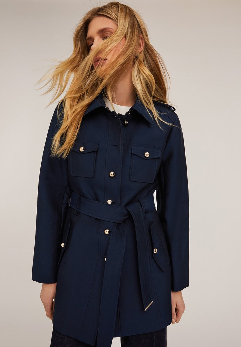 Granatowy płaszcz trench z paskiem w talii, złotymi guzikami i kieszeniami z przodu. Zaprojektowany z kołnierzem i prostym krojem.
