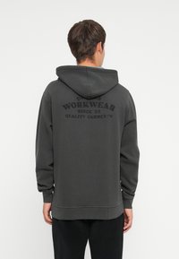 Hanorac gri cu buzunar tip cangur, având inscripția "WORKWEAR SINCE '22" imprimată cu litere negre îngroșate pe spate. Material moale și croială lejeră.