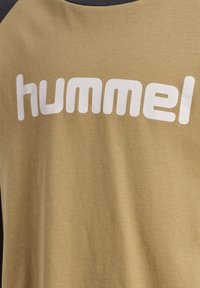 Olivgrön t-shirt med rund halsringning som har "hummel"-logotypen i fet vit text, tillverkad av mjuk bomullsjersey.