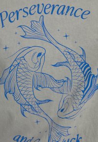 Camiseta gráfica con dibujos en línea azul de dos peces koi sobre una tela de color gris claro, con el texto "Perseverancia y buena suerte."