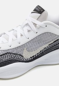 Hvide sportssko med mesh- og stofoverdel i grå nuancer, præget af en sort tekstureret sål og et beige Nike swoosh-logo.