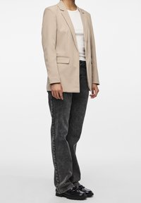 Beige blejzr s klopovými límci přes bílý ribbrový top, doplněný o šedé džíny s vysokým pasem a černé platformové boty. Viditelné hladké textury.