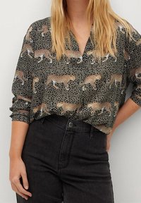 Schwarz-weiße Bluse mit Leopardenmuster, lockerer Schnitt, Knopfleiste und aufgerollten Ärmeln. Weicher, strukturierter Stoff.