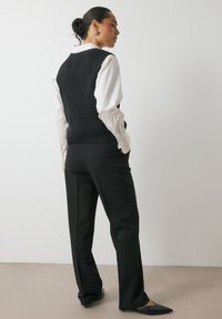 Chaleco de punto acanalado negro sobre una camisa blanca con cuello, combinado con pantalones negros ajustados y bailarinas de punta. Diseño moderno y sencillo.
