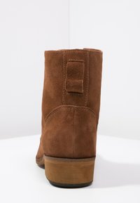 Bottines en daim marron avec une surface texturée, une petite languette à l'arrière et un talon en bois. Le design présente des lignes fluides et une forme arrondie.
