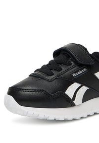 Atletska crno-bijela cipela s gornjim dijelom od kože, vezicama i kopčanjem na velcro, teksturiranim potplatom i prepoznatljivim bočnim prugama.