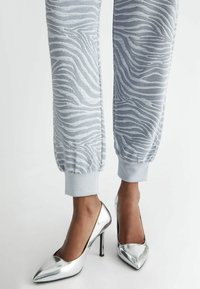 Lys grå joggers med et zebra-stribe mønster og elastiske manchetter, parret med skinnende sølv stiletter med spidse tæer.