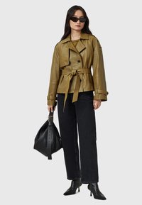 Giacca di pelle verde oliva con vita aderente, chiusura doppiopetto e ampi revers. Abbinata a jeans neri a gamba larga e décolleté a punta.