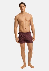 Shorts de bain rouges à motif géométrique, avec une taille élastique et une texture légère, portés par un mannequin torse nu.
