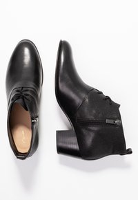 Botas negras hasta el tobillo de cuero con punta redondeada, cremallera lateral, acentos texturizados y tacón ancho. Presenta detalles de encaje en la parte frontal.