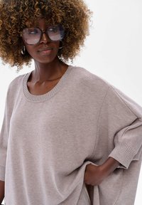 Jasno beżowy, oversize sweter z prążkowanym dekoltem i mankietami. Miękka tekstura, rękawy w kształcie nietoperza oraz boczne rozporki dla dodatkowego komfortu i stylu.