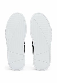 Czarne podeszwy sneakersów z fakturowanej białej gumy, charakterystyczne logo oraz skośne rowki dla lepszej przyczepności. Prosty design, bez dodatkowych akcentów.