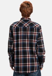 Czarna, czerwona, biała i niebieska flanelowa koszula w kratę z długimi rękawami i kołnierzykiem na guziki. Posiada prosty dół oraz design z yoke z tyłu.