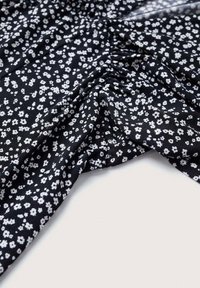 Tissu noir orné d'un motif floral blanc éparpillé. Le matériau est doux avec une légère texture, tombant délicatement avec des sections froncées.