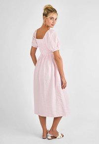 Ružičasta gingham midi haljina s napuhanim rukavima i kvadratnim izrezom. Ima gumirani struk i lepršavu suknju. Nosena s ravnim sandalama.