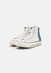 High-Top-Sneaker aus weißem Canvas mit blauen und schwarzen Seitenstreifen, Schnürung vorne, Gummisohle und strukturierter Zehenkappe.