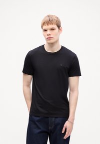 Black cotton t-shirt with round neckline and short sleeves, featuring a small logo on the left chest, paired with blue jeans.
