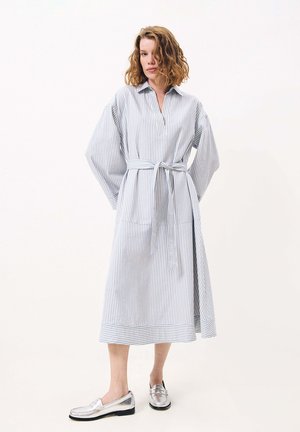 Gestreiftes Baumwollhemdkleid in Hellblau und Weiß mit Kragen, langen Ärmeln, einem Taillengürtel und einer lockeren Silhouette, kombiniert mit silbernen Slippern.