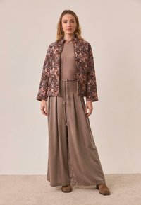 Chaqueta acolchada floral en rosa y gris, top beige de canalé, pantalones sueltos en taupe con cordón, y botines marrones.