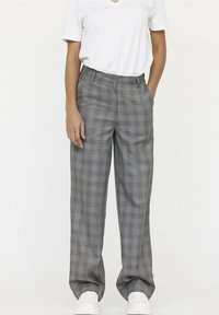 Grijze geruite broeken met een losse pasvorm, medium taille en zijzakken. Draagt een witte V-hals t-shirt en witte sneakers.