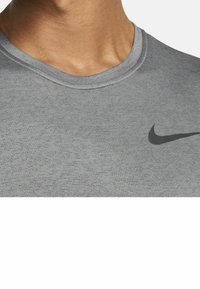 Grå kortärmad Nike t-shirt med rundad hals, texturerad tyg och en svart Nike-logotyp på vänster bröst.