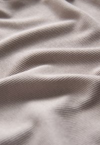 Tissu brun clair texturé avec un subtil nervurage diagonal, présentant des plis doux et fluides ainsi qu'une surface lisse.