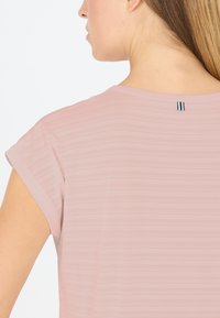 Vaaleanpunainen, lyhythihainen paita, jossa on pehmeä, teksturoitu kangas ja vaakasuorat raidat. Takana kaula-aukon kohdalla on pieni musta ja valkoinen etiketti.