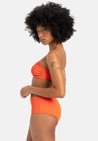 Pruhované oranžové bikiny, ktoré obsahujú bandeau vršok a vysokopáskové spodné nohavičky. Hladká textúra, jednofarebný dizajn, minimalistický bez ozdôb.
