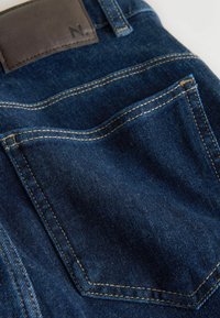 Tumesiniste teksade tagatasku kollase õmbluse ja pruuni nahast plaastri sildiga vöökohal.