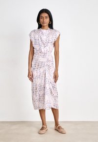 Midi dress in lightweight fabric, featuring a pink base with a colorful drop pattern, gathered waist, and cap sleeves. Paired with beige shoes.