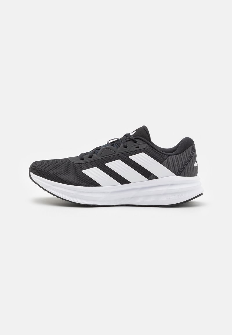 Baskets noires de sport avec semelle blanche, texture en mesh et trois bandes blanches sur le côté, vue de gauche sur fond uni.