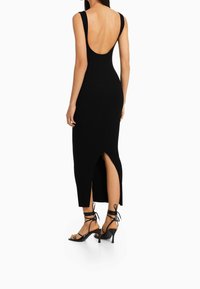 Mustavärinen ribbikuosinen maksimekko, jossa syvä pyöreä selkäaukko, sivuhalkio ja leveät olkaimet. Yhdistetty mustiin, remmikkäisiin korollisiin sandaaleihin.