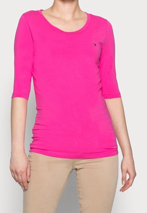 Fitted top in bright pink, lightweight fabric, scooped neckline, three-quarter sleeves, with a small logo on the left chest.