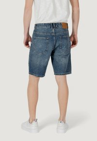 Shorts in denim blu scuro con una vestibilità ampia, orlo grezzo e cinque tasche. Dettagli scoloriti e una toppa in pelle beige sul retro.