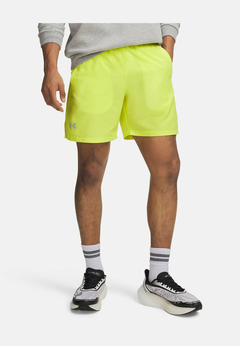 Man wearing bright yellow athletic shorts, gray sweatshirt, white socks with stripes, and black-and-white running shoes on plain background.