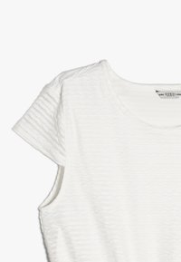 Vit kortärmad topp med texturerat diamantmönster, rund halsringning och mjukt tyg. Tagg synlig på insidan av kragen.