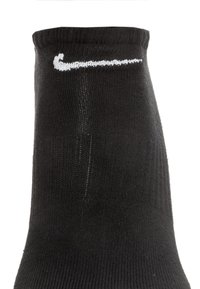Schwarze Sportsocke mit geribbelter Textur, mit einem weißen Nike-Logo nahe der Oberseite. Standard Crew-Länge-Design.