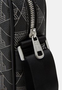 Black textured bag with a geometric pattern, featuring a metallic zipper, silver hardware, and a black adjustable strap.