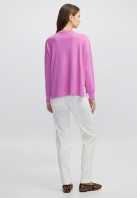 Oversized roze trui met verlaagde schouders, geribbelde manchetten, zijsplitten, gecombineerd met witte broeken en schoenen met een luipaardprint.