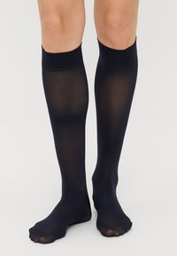 Meias até ao joelho em preto, feitas de material transparente, com uma textura suave e um elástico apertado na parte superior, apresentando um design de ponta aberta.