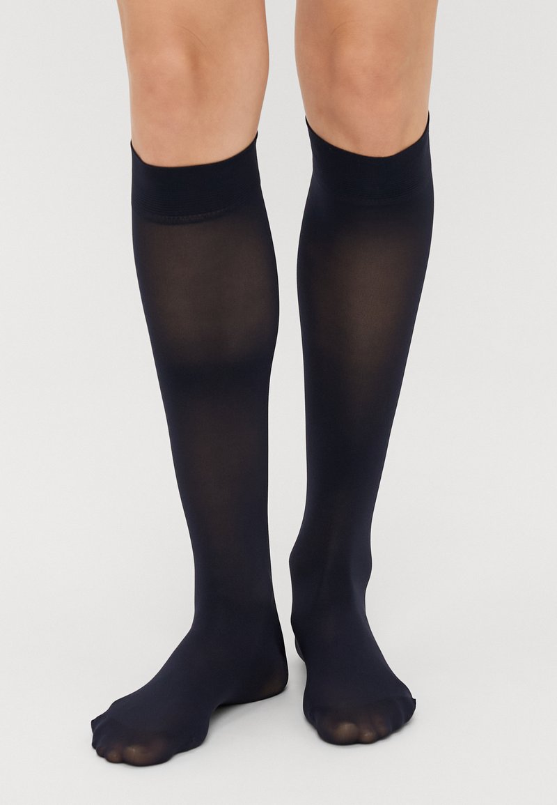 Meias até ao joelho em preto, feitas de material transparente, com uma textura suave e um elástico apertado na parte superior, apresentando um design de ponta aberta.