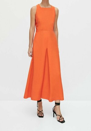 Pomarańczowa sukienka midi bez rękawów z kwadratowym dekoltem i plisą z przodu, noszona przez modelkę w czarnych sandałkach na wysokim obcasie z paskami.