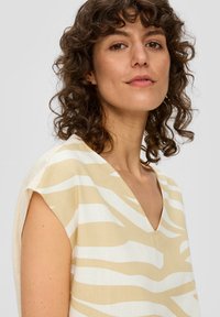 Leichtes, beiges Oberteil mit weißen Zebrastrichen. V-Ausschnitt-Design mit kurzen Ärmeln und einem glatten, strukturierten Stoff.