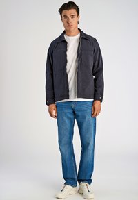 Granatowa kurtka z kołnierzem, dwoma kieszeniami na piersi i zamkiem błyskawicznym, zestawiona z jasnoniebieskimi dżinsami i białymi trampkami. Prosty design, teksturowana tkanina.