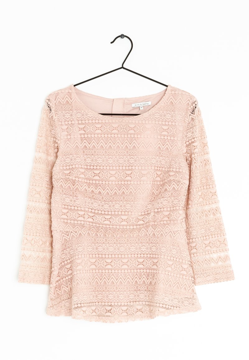 Haut en dentelle rose pâle à manches longues, présentant un motif texturé de fleurs et de designs en zigzag. Encolure ronde et ourlet festonné.