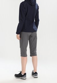 Marinblå huva jacka och grå knälånga shorts. Idrottsskor i svart och grått. Slät tyg med sömnadsdetaljer.