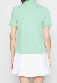 Polo de color verde menta con mangas cortas enrolladas, presenta un cuello clásico y una tela suave y ligera. Combinado con una falda blanca.