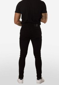 Vaqueros ajustados negros con textura suave, cintura de talle medio y diseño de cinco bolsillos. Combinados con una camiseta negra y zapatillas blancas.