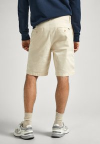 Beige bomullsshorts i avslappnad passform, med två bakfickor och subtila sömmar. Matchade med grå sneakers och ljusa strumpor.