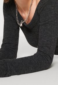 Grauer gestrickter Pullover mit einer weichen Textur und weitem Ausschnitt, akzentuiert durch eine silberne Kettenhalskette mit einem Anhänger.